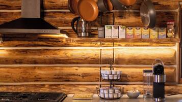 A kitchen with a wooden wall, hanging pots, a coffee machine, and a stove.