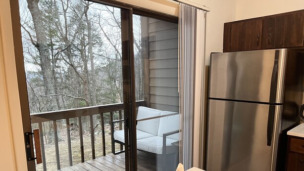 A kitchen with a stainless steel refrigerator, a wooden table with a white cushion, and a sliding glass door leading to an outdoor deck with a wooden railing. - Wintergreen 1bed Condo, Walk to slopes, close to Hiking, Breweries, Wineries (Wintergreen Resort)