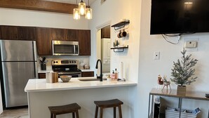 A modern kitchen with stainless steel appliances, wooden cabinets, and a central island with stools. - Wintergreen 1bed Condo, Walk to slopes, close to Hiking, Breweries, Wineries (Wintergreen Resort)