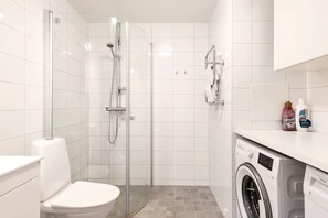 A modern bathroom with a glass-enclosed shower, a toilet, and a washing machine.