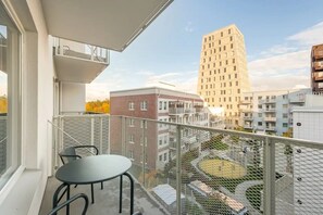 A balcony with a table and chairs, overlooking a courtyard with a tall building in the background.
