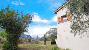Un edificio blanco con una pequeña ventana y una puerta, rodeado de follaje y un cielo despejado.