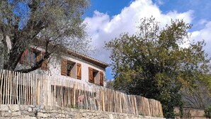 Una casa rústica con pared de piedra y cerca de madera, rodeada de árboles y un cielo despejado.