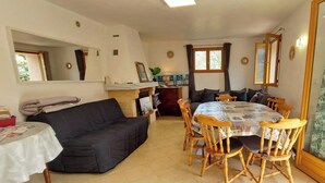 Una sala de estar acogedora con un sofá negro, una mesita y un comedor con sillas de madera y mantel estampado.