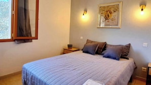 Un dormitorio con cama, mesita de noche, lámpara de pared y un cuadro enmarcado.