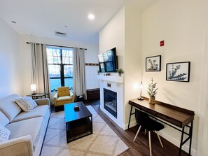 A modern living room with a sofa, a coffee table, a TV, a fireplace, and a desk.