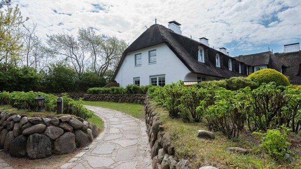 A white house with a black roof, surrounded by a stone wall and greenery. - House Ameland, App. 3 - Modern 3-room apartment with approx. 85m² living space, (Wenningstedt-Braderup (Sylt))