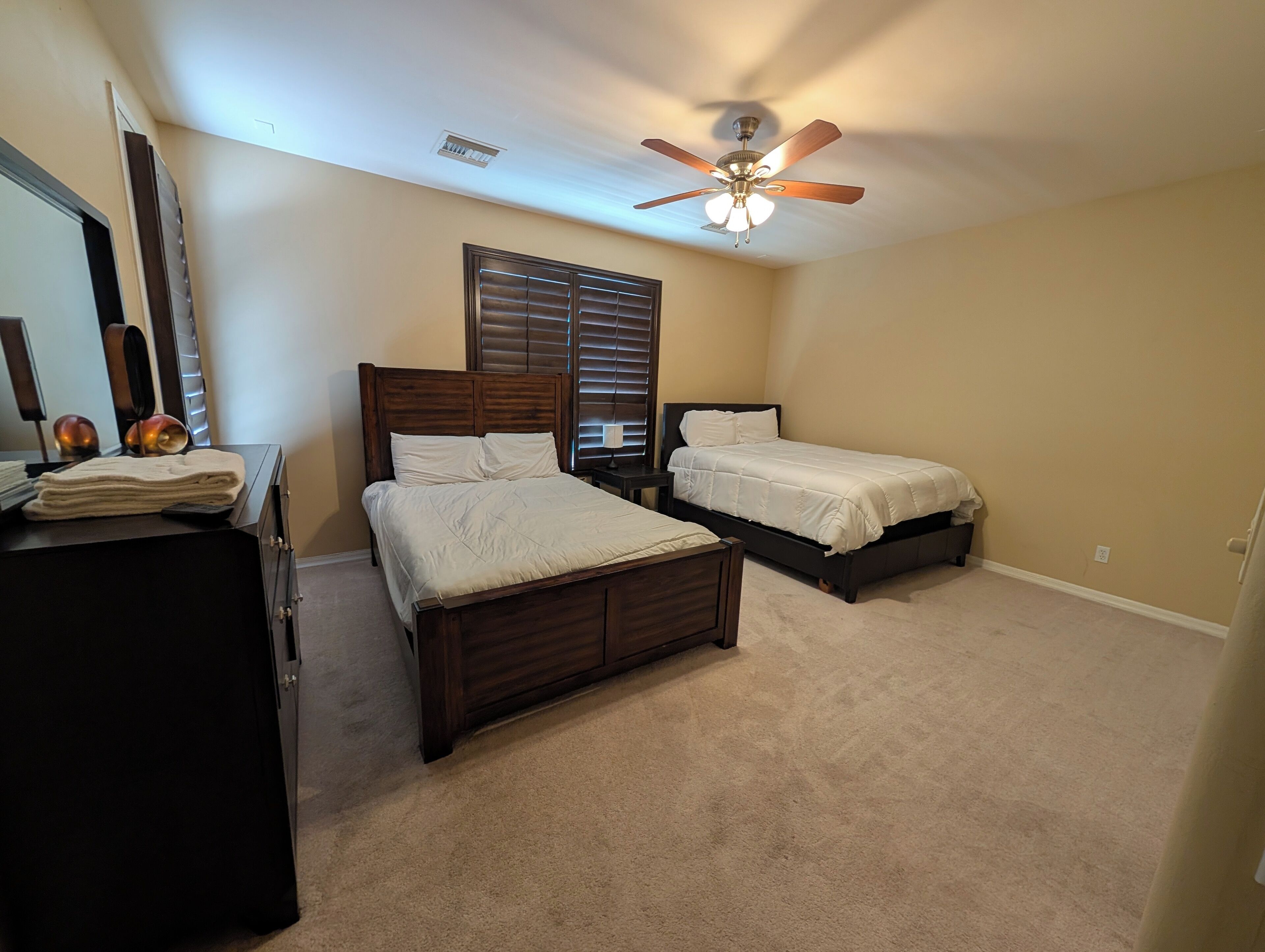 A bedroom with two beds, a ceiling fan, and a dresser.