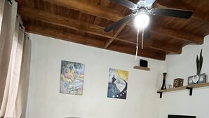 Una sala de estar con techo de madera, ventilador de techo, sofá, mesa de centro, televisor sobre un mueble bajo y obras de arte en las paredes.