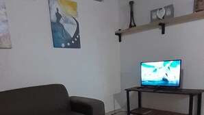 Una sala de estar con un sofá, una mesa de centro de madera, un televisor sobre un mueble bajo y obras de arte en las paredes.