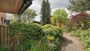A brick pathway leading through a garden with various plants and a tall evergreen tree. - Haus Ersfeld – Garden Apartment with Private Terrace, Shared Garden, and Wi-Fi (Bad Teinach-Zavelstein)