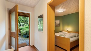 A bedroom with a wooden bed, a bedside table, a nightstand, a wall-mounted picture, and a door leading to a garden. - Haus Ersfeld – Garden Apartment with Private Terrace, Shared Garden, and Wi-Fi (Bad Teinach-Zavelstein)
