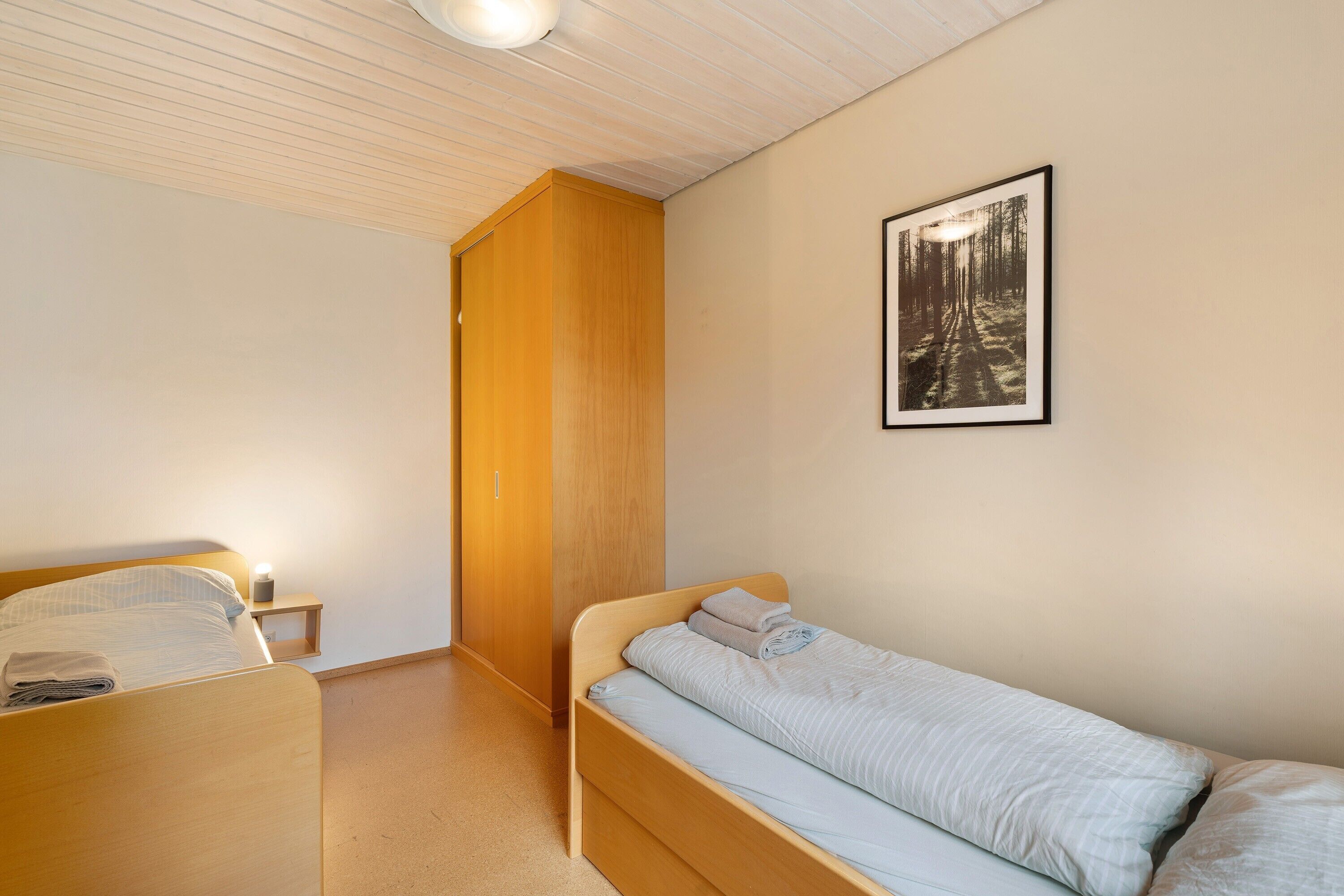 A bedroom with a single bed, a nightstand, a wooden wardrobe, and a framed picture on the wall.