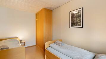 A bedroom with a single bed, a nightstand, a wooden wardrobe, and a framed picture on the wall.
