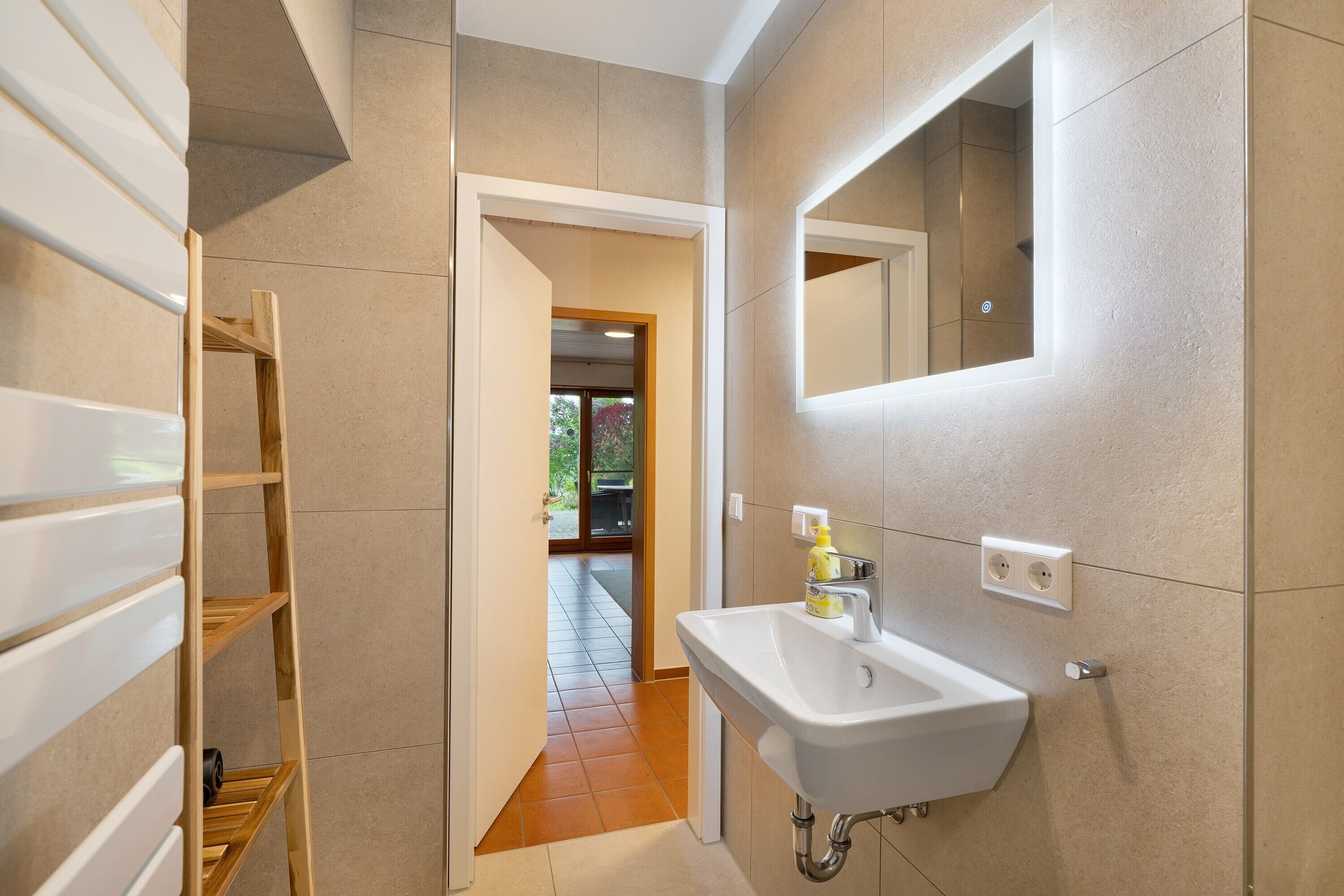 A bathroom with a white sink, a mirror, and a wooden shelf.