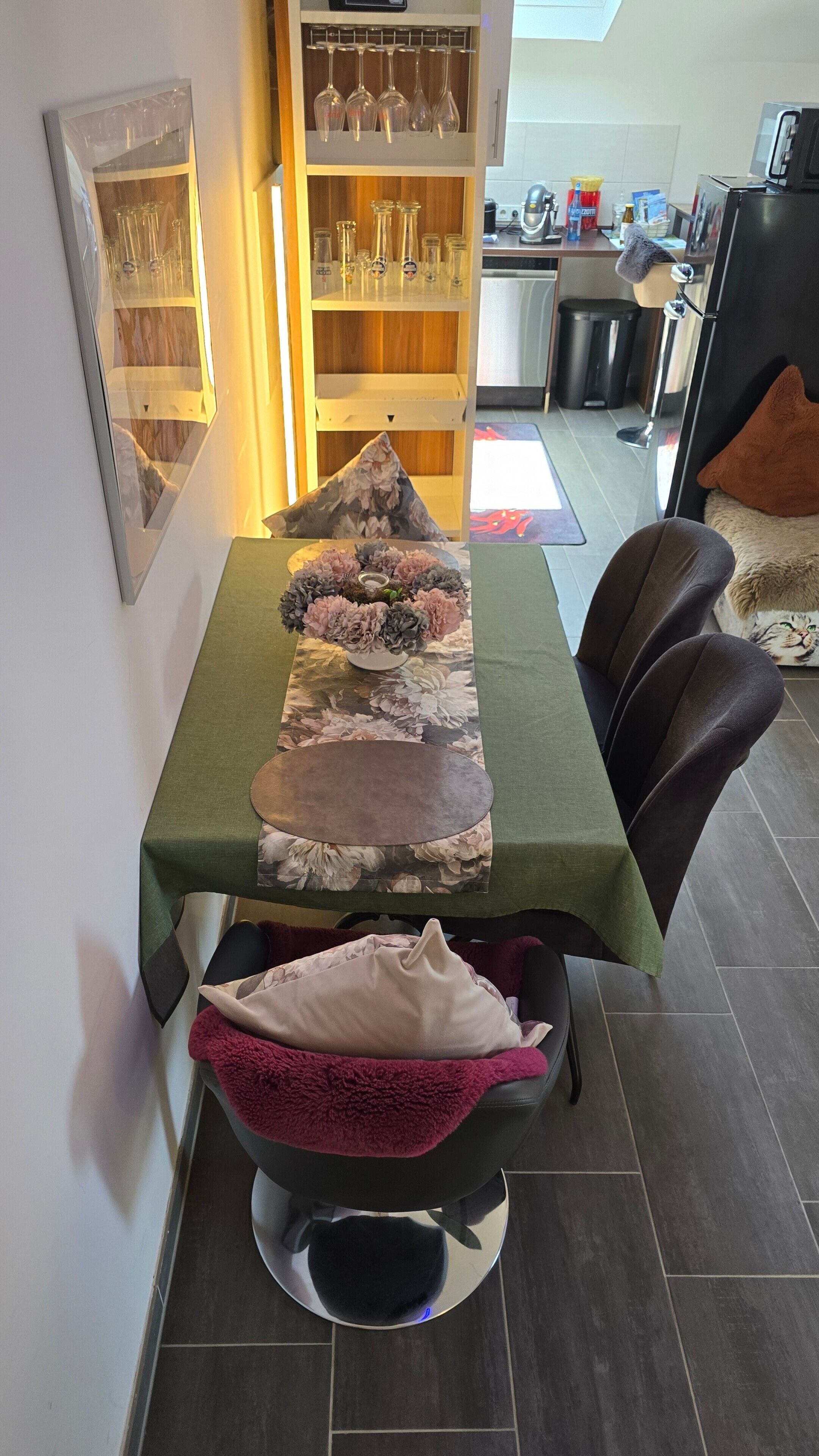 Un coin repas avec une table dressée pour deux personnes, un panier pour animaux de compagnie et un animal visible.