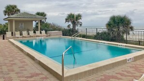 Piscina rectangular con borde de azulejos, rodeada por una valla baja y palmeras.