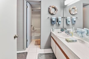 Un baño moderno con ducha, lavamanos e inodoro. Hay toallas colgadas en la pared y una guirnalda decorativa sobre el espejo.