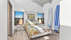 Un dormitorio moderno con una cama, un ventanal grande y tablas de surf apoyadas en la pared.