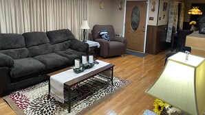 Un salon avec un canapé gris foncé, un fauteuil marron, une petite table avec des bougies et un tapis à motifs.