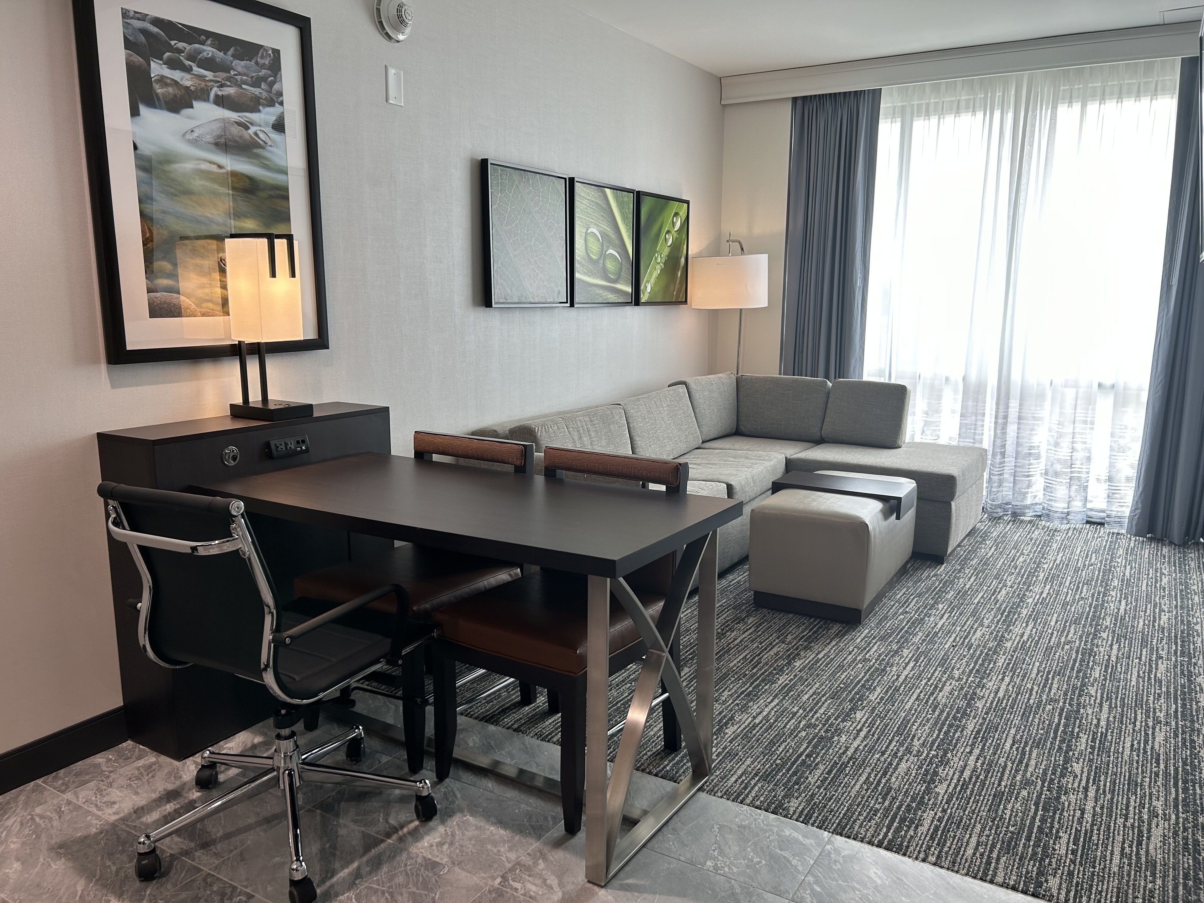 A hotel room with a desk, office chair, sofa, and a large window with curtains.