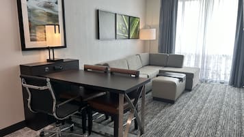 A hotel room with a desk, office chair, sofa, and a large window with curtains.