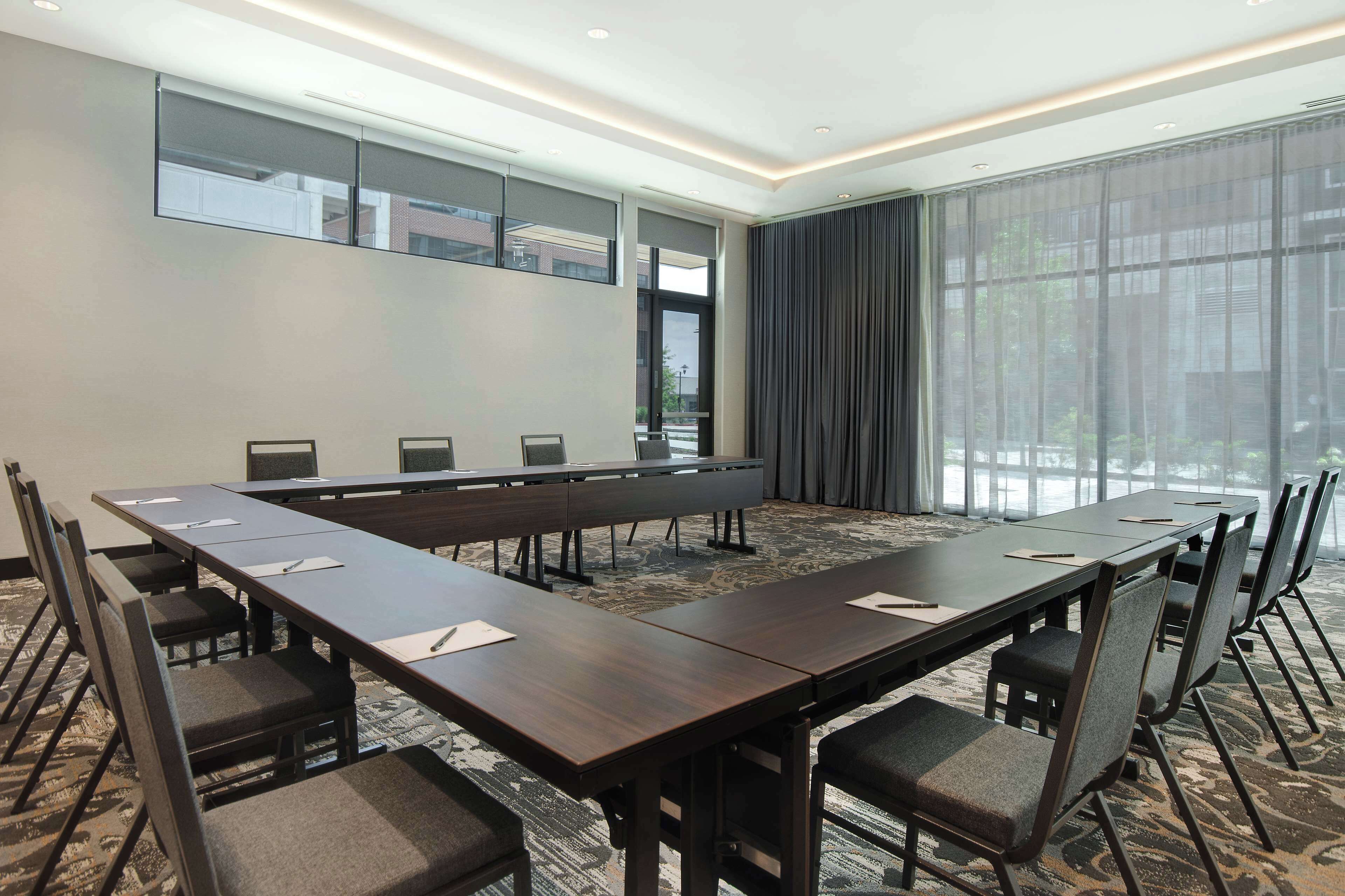 A conference room with a long table, chairs, and a large window with curtains.
