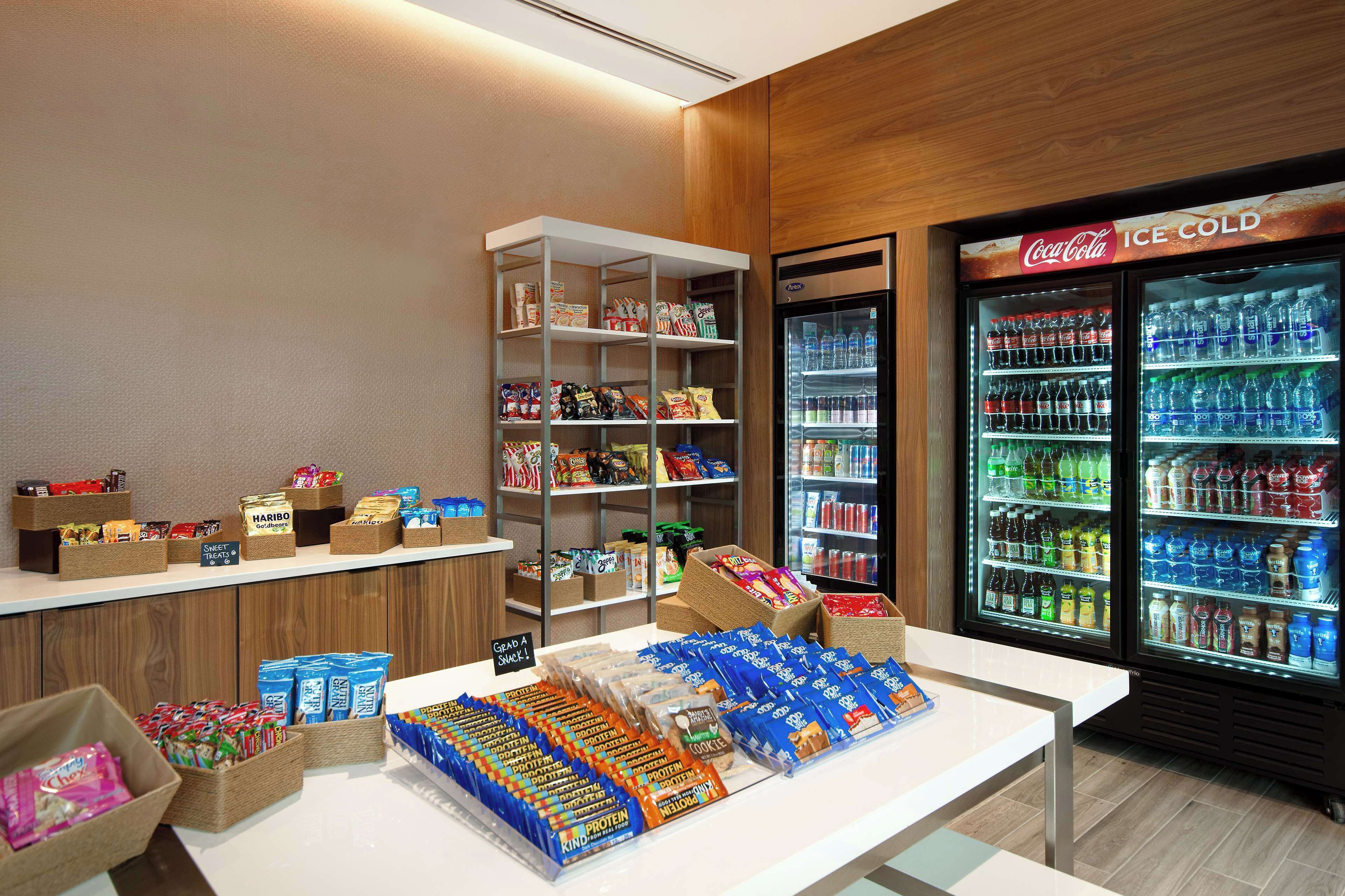 Zona de exhibición de aperitivos y bebidas, con estantes llenos de productos y un refrigerador Coca-Cola bien frío.