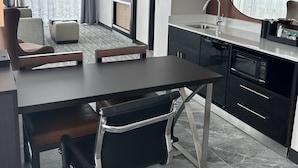 A modern hotel room with a dining area, a flat-screen TV mounted on the wall, a large mirror, and a kitchenette. - Embassy Suites By Hilton Alpharetta Halcyon (Alpharetta)