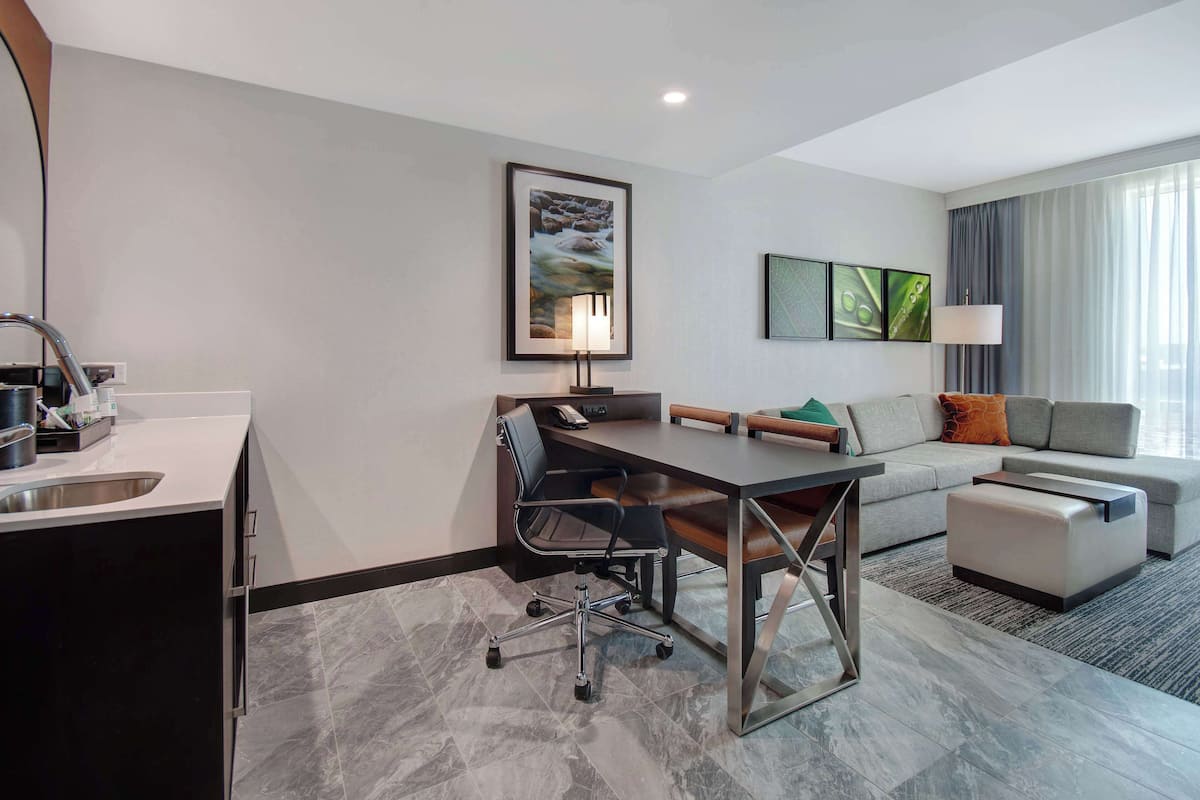 A modern hotel room with a dining area, a sofa, and a desk.
