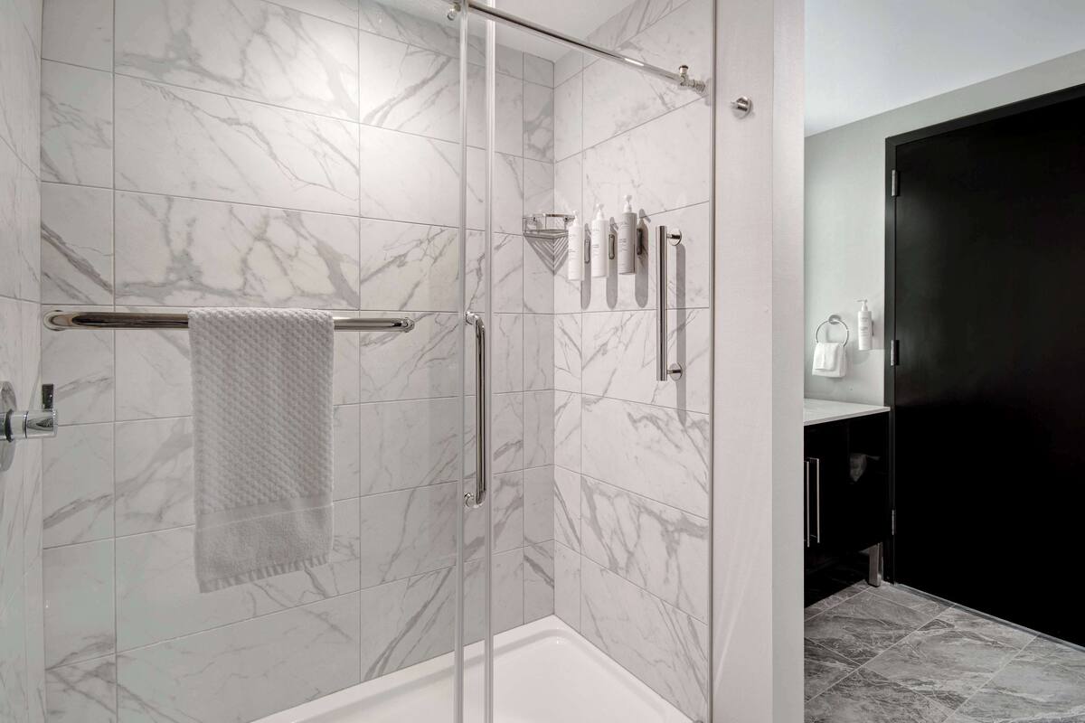A modern bathroom with marble tiles, a glass shower enclosure, a towel rack, and a dark cabinet.