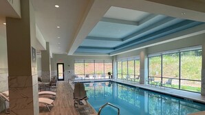 An indoor swimming pool with a wooden deck, lounge chairs, and large windows offering a view of the outdoors. - Embassy Suites By Hilton Alpharetta Halcyon (Alpharetta)