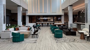 A spacious lobby with a central bar area, seating arrangements, and a modern chandelier. - Embassy Suites By Hilton Alpharetta Halcyon (Alpharetta)