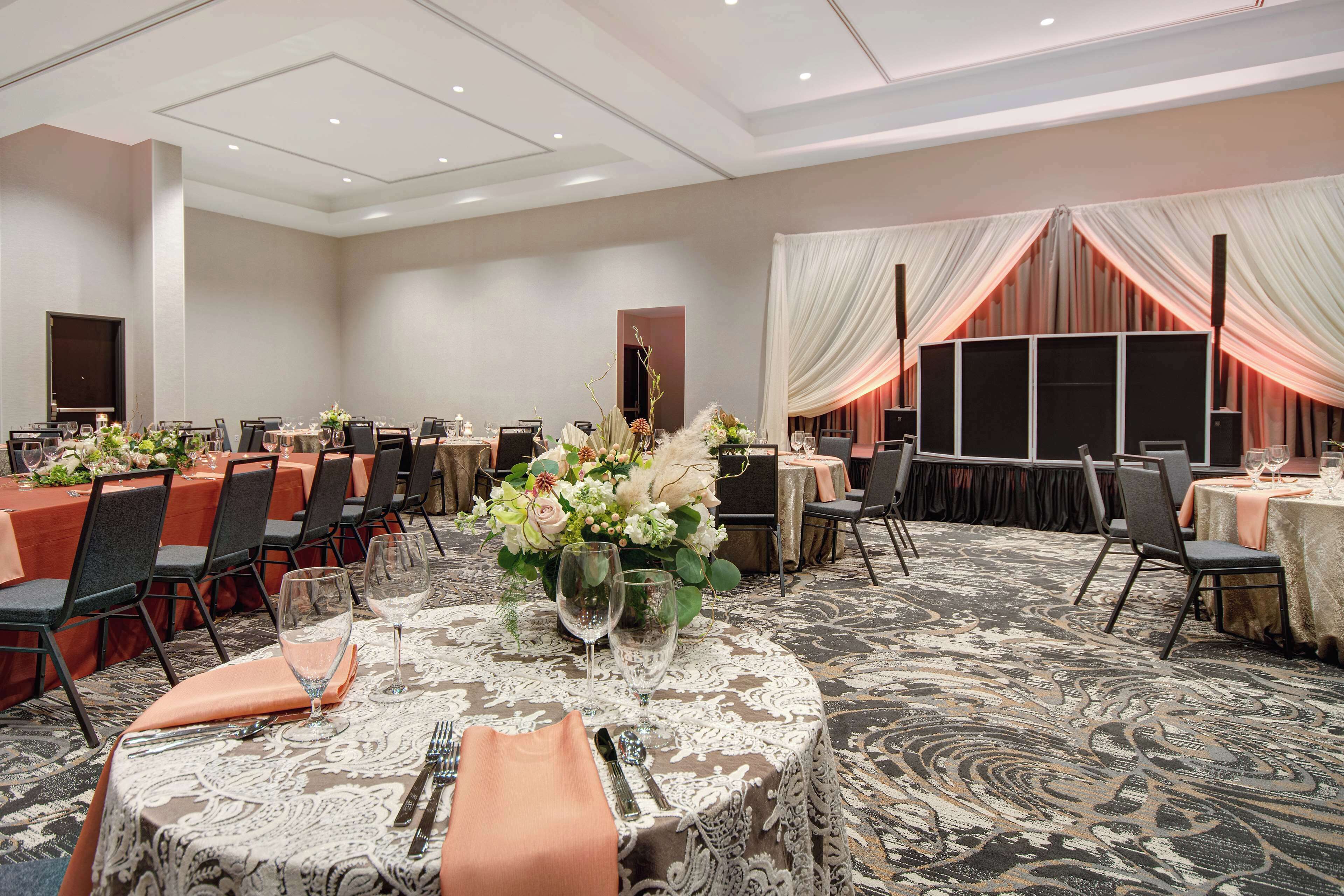 A banquet hall with round tables, chairs, and floral centerpieces.