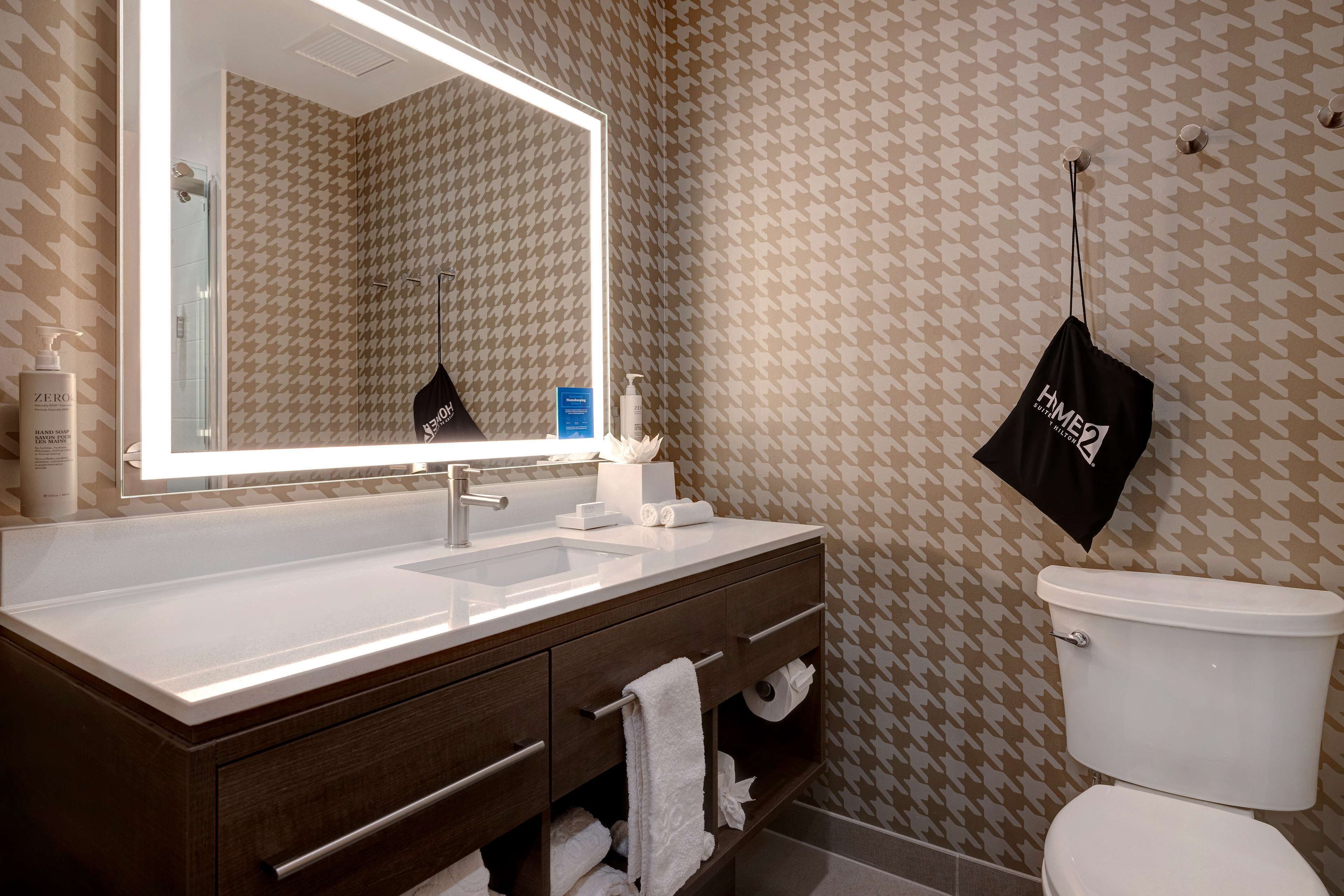 A bathroom with a large mirror, a white sink, a dark wooden vanity, and a toilet.