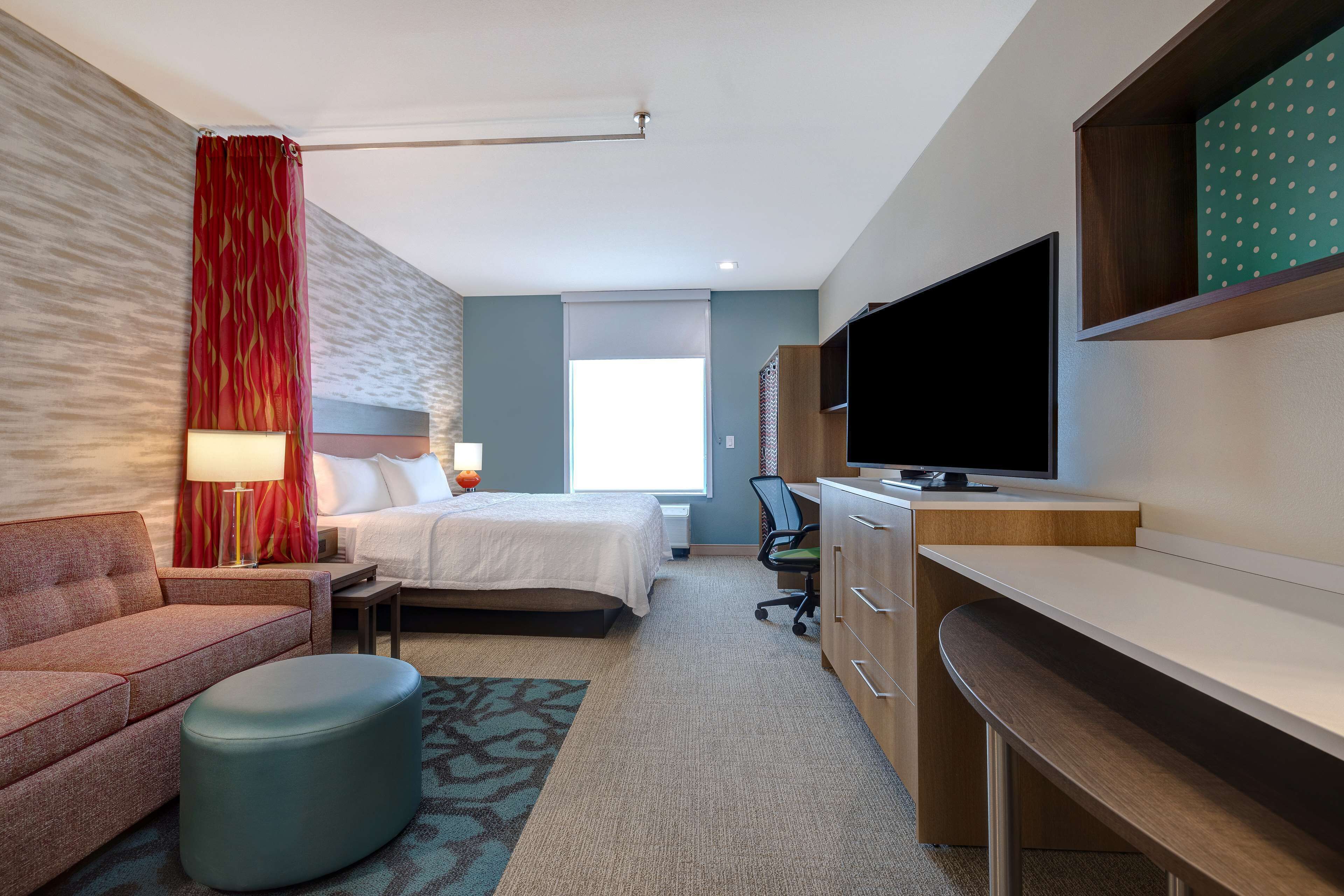A hotel room with a bed, a desk, a television, a sofa, and a patterned rug.