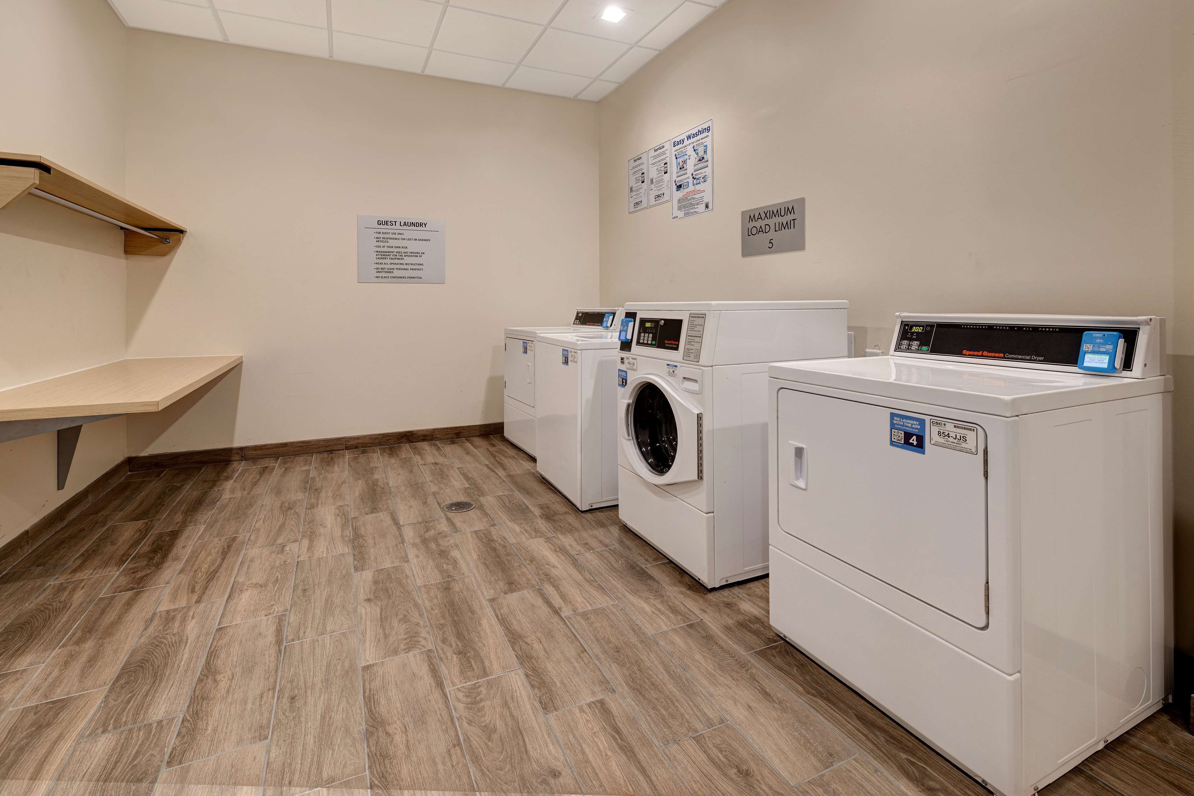 A laundry room with two front-loading washers and dryers, a wooden bench, and a sign indicating guest laundry facilities.