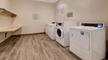 A laundry room with two front-loading washers and dryers, a wooden bench, and a sign indicating guest laundry facilities.