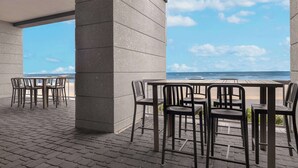 Een terras buiten met tafels en stoelen, met uitzicht op een strand.