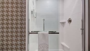 A shower area with white tiled walls, a glass door, and a towel hanging on a rack.