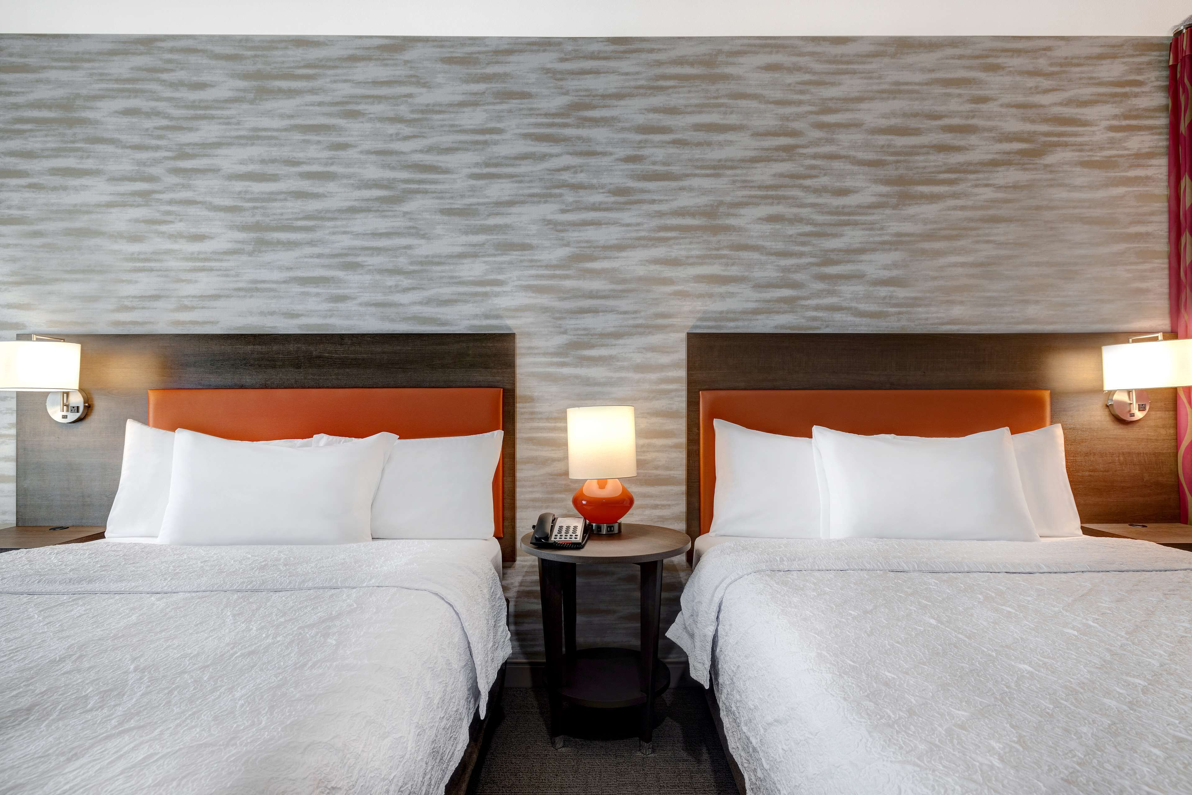 A hotel room with two beds, a round table with a lamp, and a textured wall.