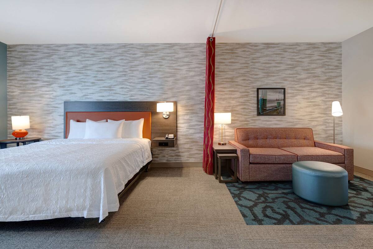Een hotelkamer met een bed, een bank, een tafeltje, een lamp en een foto aan de muur.