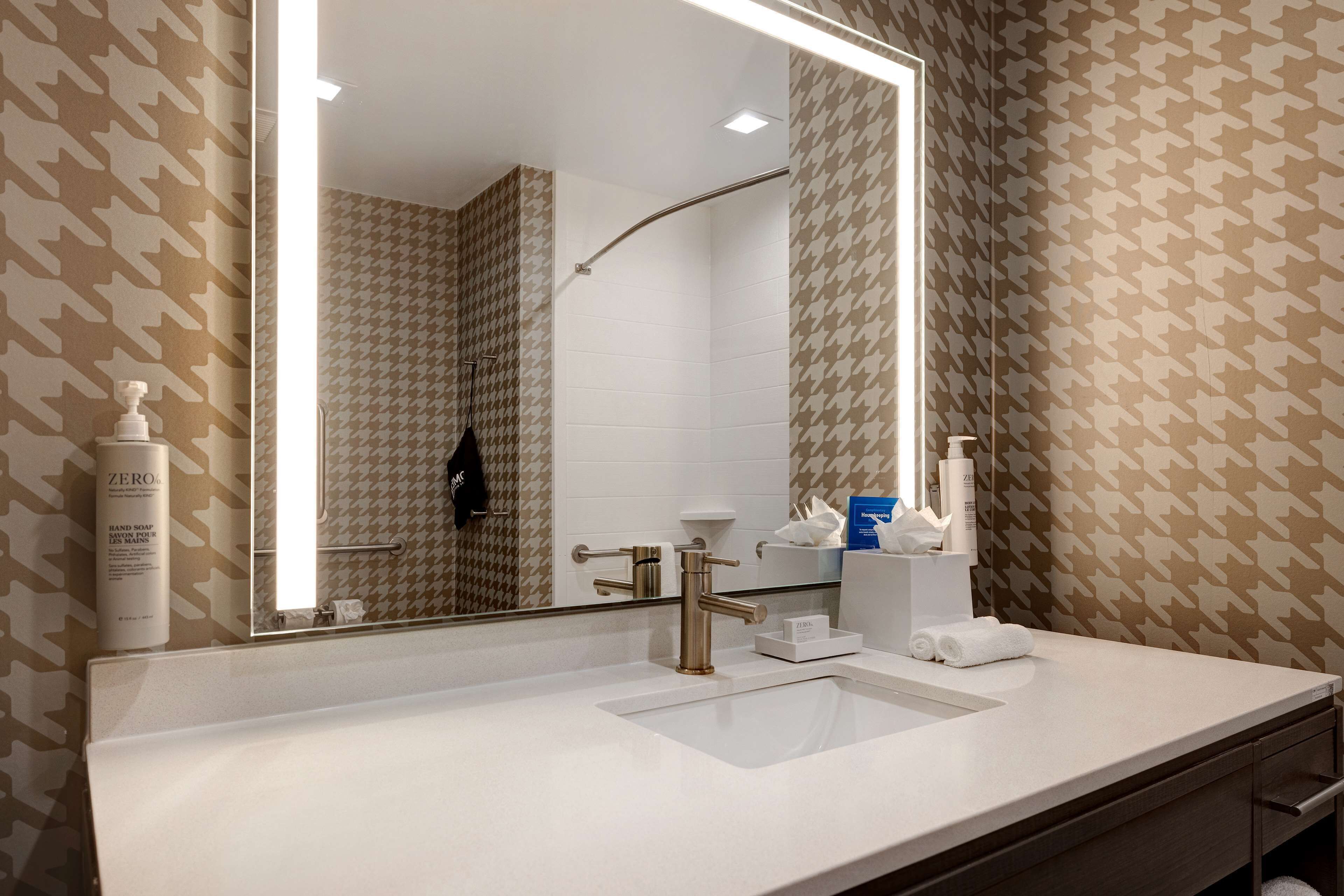 A modern bathroom with a large mirror, a sink, and a shower.