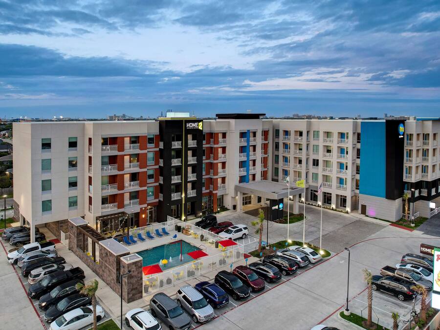 Un hôtel à plusieurs étages doté d'une piscine sur le toit, d'un parking et d'une enseigne « Papa's Pizza ».
