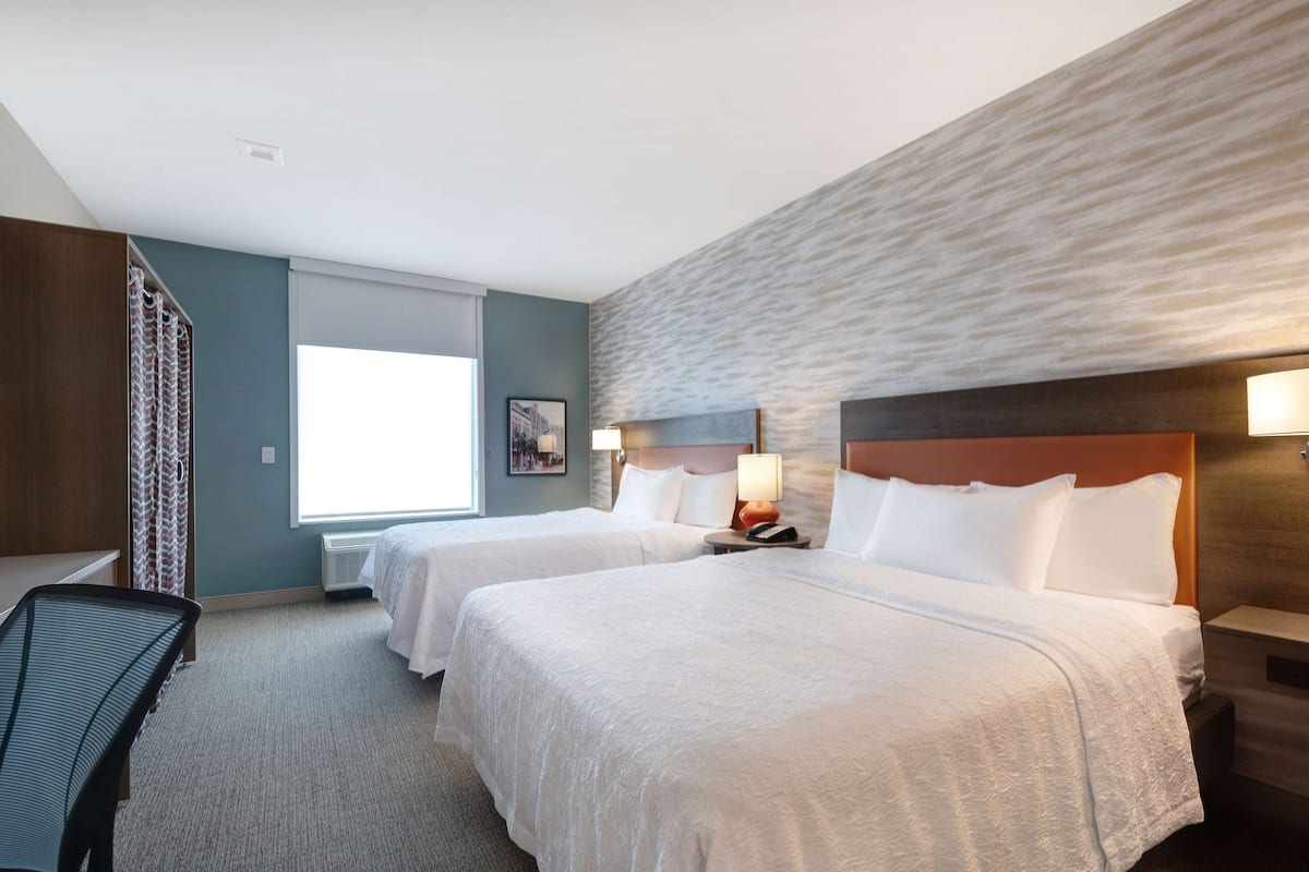 Een hotelkamer met twee bedden, een bureau, een stoel, een raam met gordijnen en een gestructureerde wand.