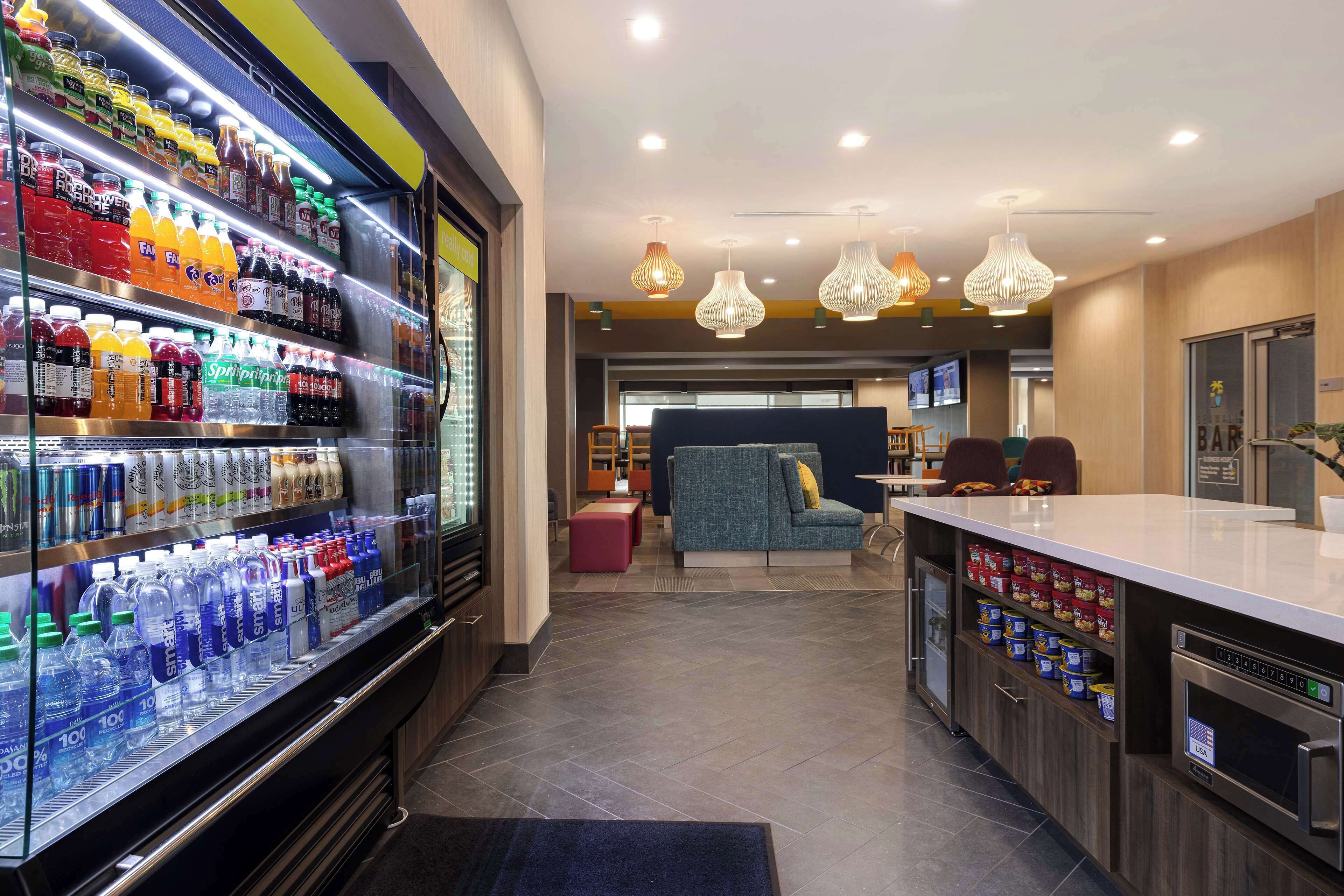 A modern hotel lobby with a refrigerated beverage display, seating area, and a kitchenette.