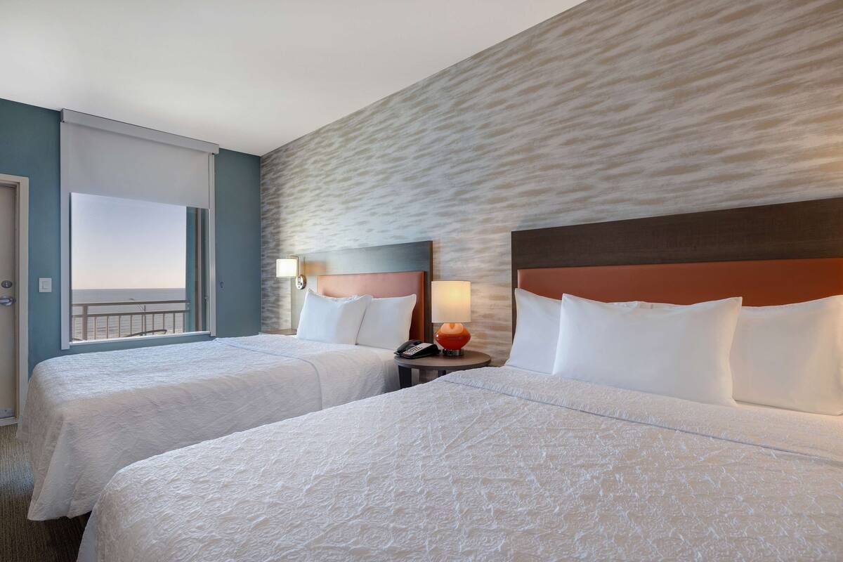 Een hotelkamer met twee bedden, uitzicht op de oceaan en een structuurwand.