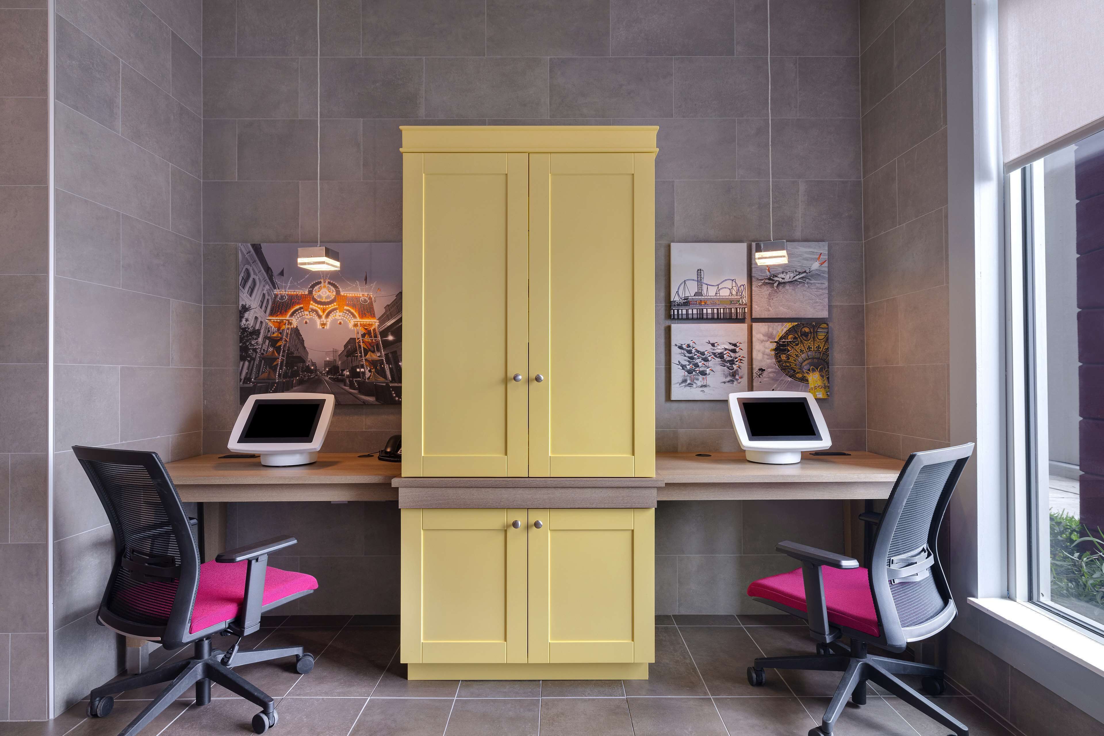 Un espacio de oficina moderno con dos escritorios, cada uno con un monitor de computadora, dos sillas de oficina y un armario amarillo grande.