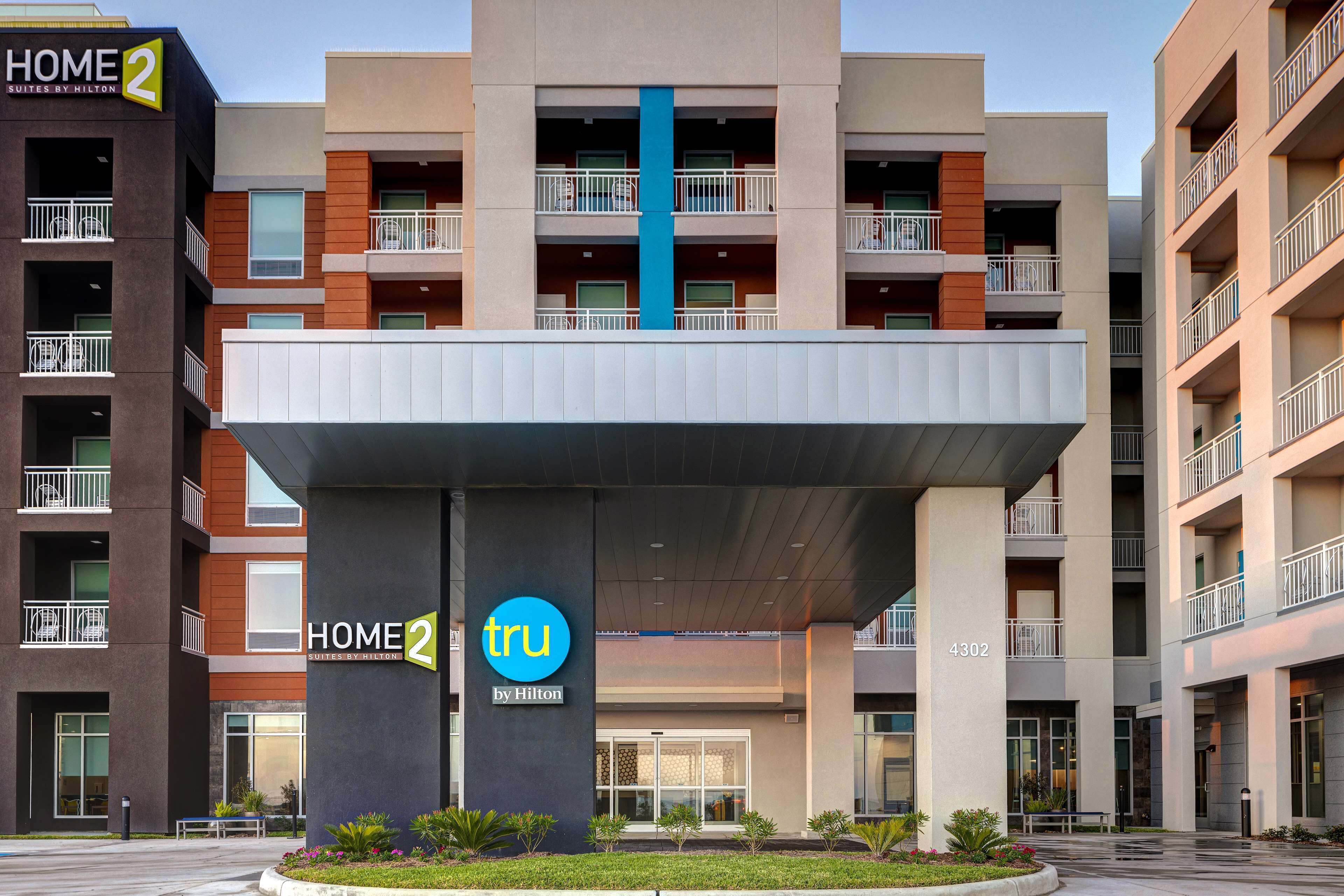 A modern hotel with a central atrium, multiple balconies, and a prominent 'Home 2 by Hilton' sign.
