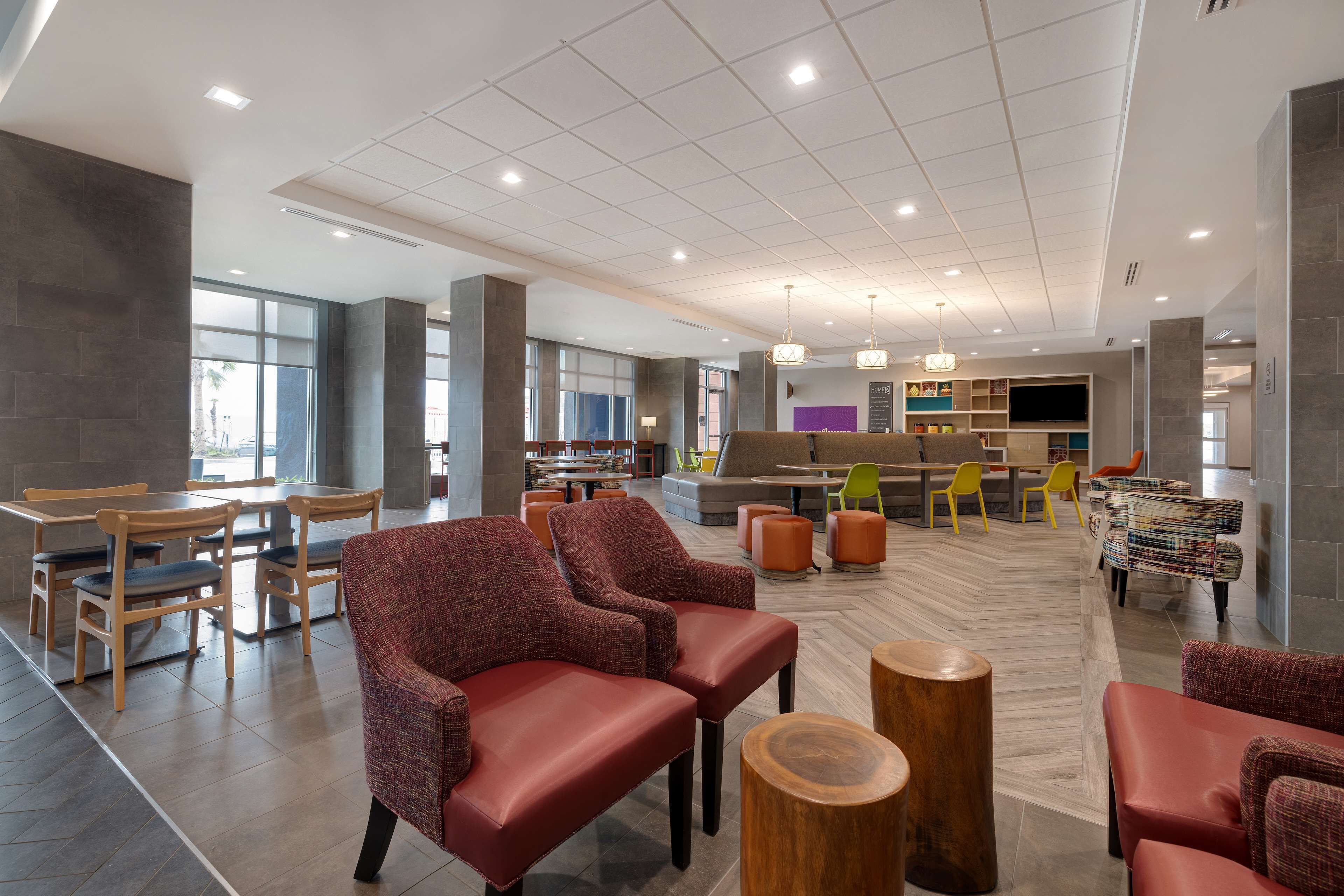 A spacious lobby with seating areas, a central coffee station, and a large flat-screen TV mounted on the wall.